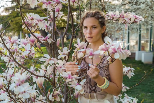 Magnolia flowers. Happy woman enjoys by blooming magnolia tree and sniffs it flowers with closed eyes in spring garden. Portrait