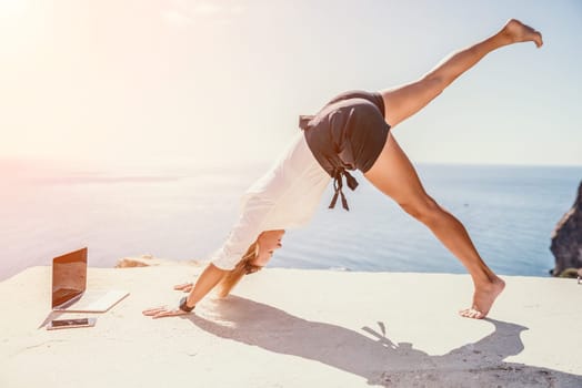 Happy girl doing yoga with laptop working at the beach. beautiful and calm business woman sitting with a laptop in a summer cafe in the lotus position meditating and relaxing. freelance girl remote work beach paradise