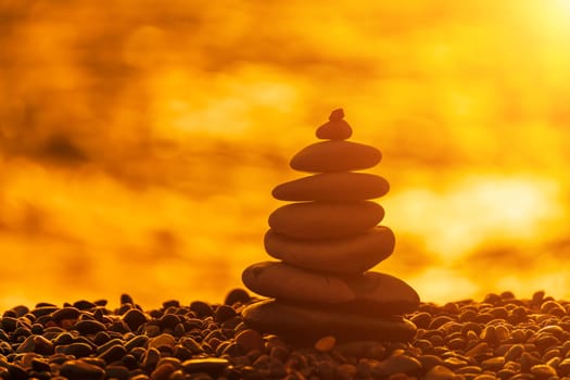 Balanced rock pyramid on pebbles beach. Golden sea bokeh on background. Selective focus, zen stones on sea beach, meditation, spa, harmony, calm, balance concept