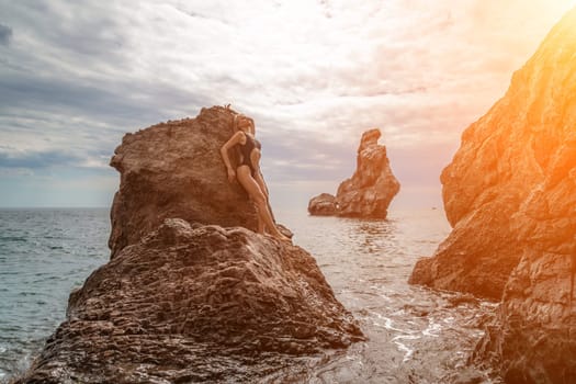 Woman swimsuit sea. Attractive blonde woman in a black swimsuit enjoying the sea air on the seashore around the rocks. Travel and vacation concept