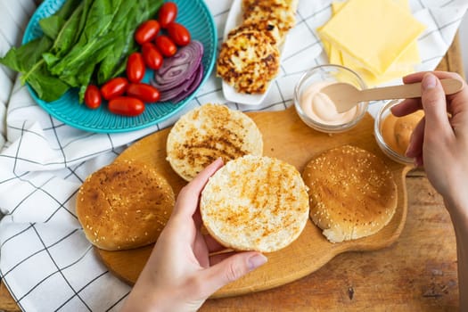 Preparation of all the ingredients for making a burger - bun, cutlet, cheese, salad, tomato, sauces. Top view, girl's hands take a burger roll