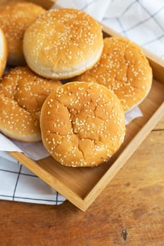 Freshly baked lush burger buns lie on a wooden tray on a table with a white napkin. Top view, close-up. Yellow flavored pastries with white sesame seeds