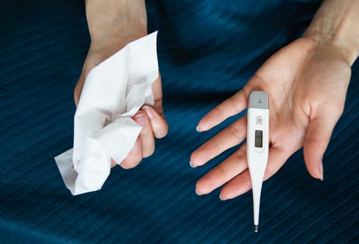 The girl holds a paper towel in her right hand and a thermometer in her left. Arms extended in front of you. The concept of self-control and self-control in viruses and epidemics.