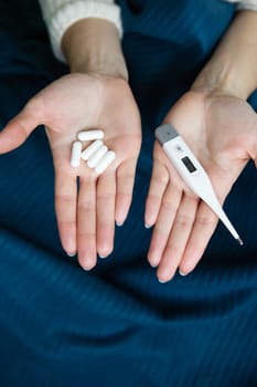 Girl holds pills in her right hand and a thermometer in her left. Arms outstretched before you. The concept of self-control and self-control in viruses and epidemics.