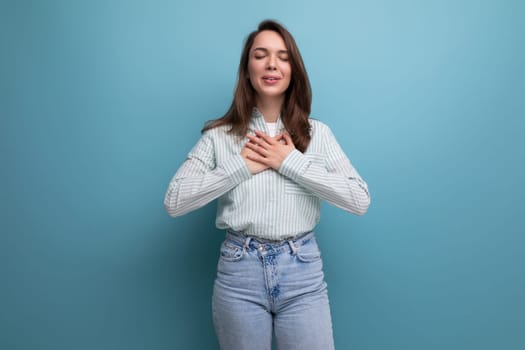 kind young brunette lady dressed in a striped shirt and jeans holds her hands to her chest.