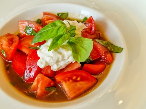 Sliced fresh Italian burrata cheese with tomato slices on a white plate on a white background.
