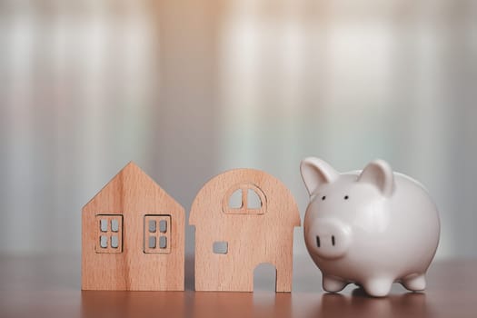Saving piggy bank with wooden house model on the table for business, finance, saving money and property investment concept.