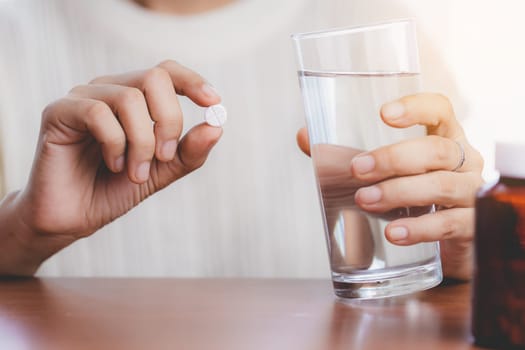 Woman's hand taking medicine pill and drinking water with the brown bottle on the table for healthcare concept.