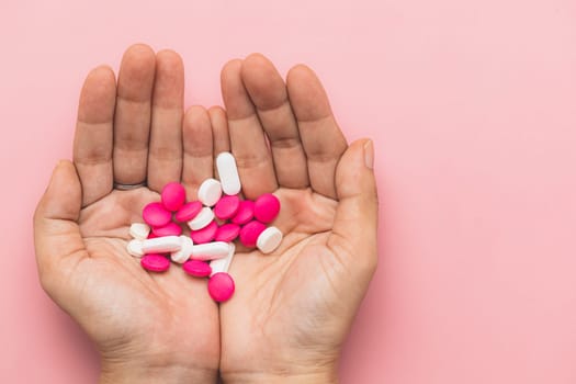 Top view of hand holding medicine pills on pink background for medical and healthcare concept.