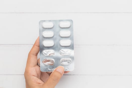 Top view of hand holding a blister pack of medicine pill on white table background for medical and healthcare concept