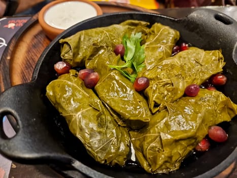 Delicious stuffed grape leaves ,traditional doom Mediterranean cuisine Dolma, on a black plate with fresh cilantro and dill on dark wooden background top view with copyspace