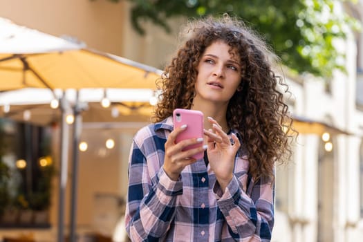 Tourist traveler pretty young woman using smartphone typing text messages looking for search a way on map in mobile navigator app outdoors. Girl walking passes by urban sunshine city street background