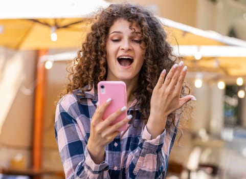 Pretty young woman use mobile smartphone celebrating win good message news, lottery jackpot victory, giveaway online outdoors. Happy girl tourist walking in urban sunshine city street. Town lifestyles