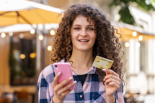 Lovely woman using credit bank card smartphone while transferring money, purchases online shopping, order food delivery, booking hotel room. Happy girl tourist walking in urban city street outdoors