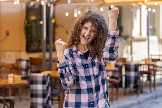 Portrait of pretty young woman shouting, celebrating success, winning, goal achievement, good news, lottery jackpot luck, victory outdoors. Girl walking in urban city sunshine street. Town lifestyles