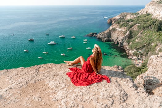 Woman sea red dress yachts. A beautiful woman in a red dress poses on a cliff overlooking the sea on a sunny day. Boats and yachts dot the background