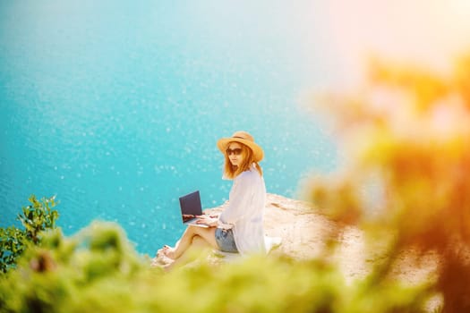 Freelance woman working on a laptop by the sea, typing away on the keyboard while enjoying the beautiful view, highlighting the idea of remote work