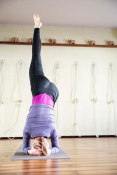 Handsome woman having yoga practice and standing on head in white lit room. Concept of physical and mental health, happy living and well being.