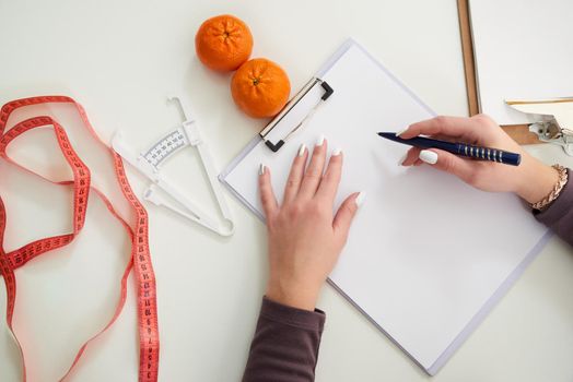 Nutritionist doctor writing diet plan on table with measuring tape, top view
