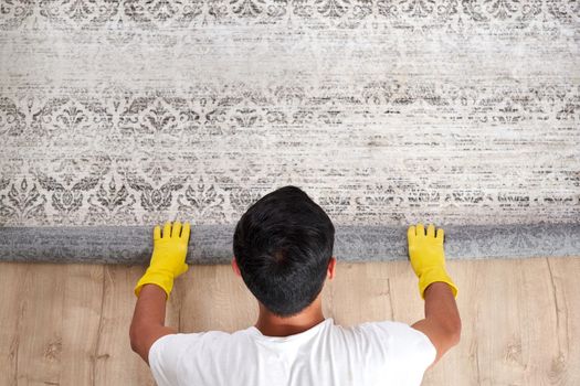 Male Worker In Overalls Rolling Carpet On Floor At Home