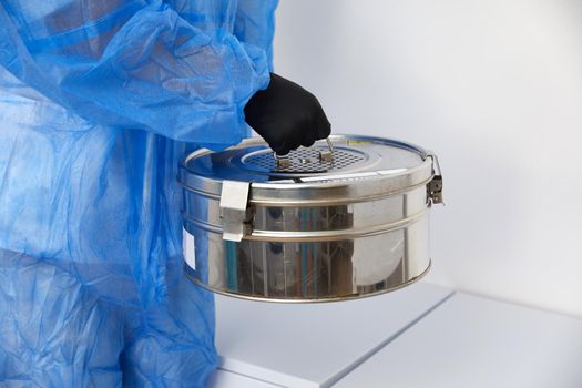 A Person standing in Laboratory holding Autoclave Sterilizer metal box wearing protective uniform