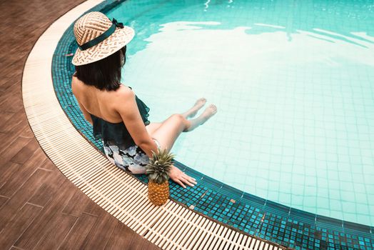 Rear View of Sexy Woman in Swimsuit Relaxing in Swimming Pool, Beautiful Woman Wearing Straw Hat and Relax on The Edge of Poolside at Resort Hotel. Summer Vacation and Relaxation Lifestyles