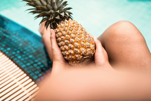 Sexy Woman is Relaxing in Swimming Pool While Holding Pineapple, Close-Up of Beautiful Woman Hold Pineapple and Relax Sunbathe in Poolside on Summer Holiday at Resort Hotel. Summer Vacation Lifestyles