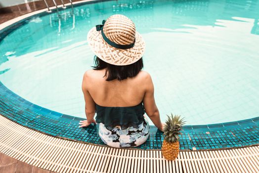 Rear View of Sexy Woman in Swimsuit Relaxing in Swimming Pool, Beautiful Woman Wearing Straw Hat and Relax on The Edge of Poolside at Resort Hotel. Summer Vacation and Relaxation Lifestyles