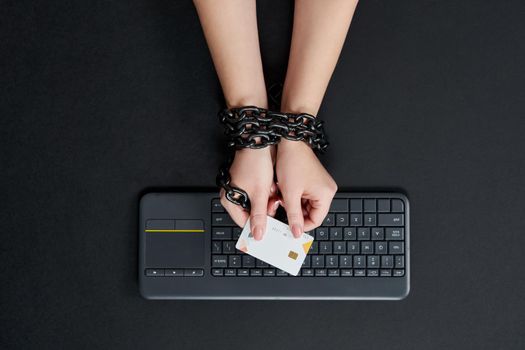 Woman with metal chain holding credit card over keyboard, online buying addiction concept