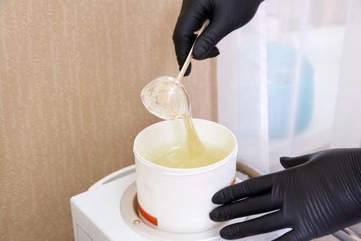 Wax for hair removal. Molten wax in a special container for heating the wax. preparing a warm Golden brow wax for hair removal.