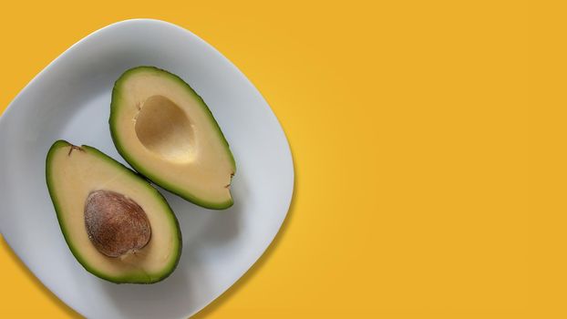 Two parts of avocado on white plate. Isolated on yellow background. 16x9 size. Template for banner with copy space at right side.