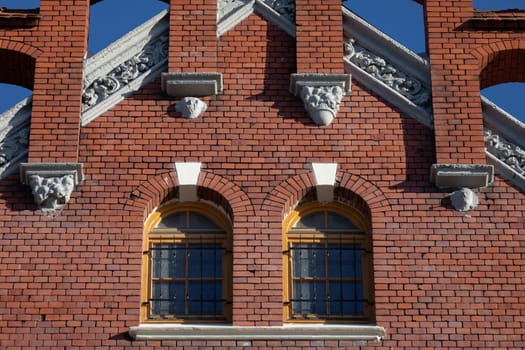 Front view of the upper gable wall of the historic red brick building. Two barred windows with an arch and decoration in the upper glyph.