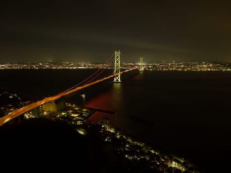 Akashi Kaikyo suspension bridge over dark water between city lights at night. High quality photo