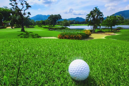 Golf ball above flag and green on tropical course in morning