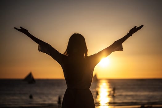 Silhouette of woman raising arms to golden sunset over sea. Freedom, success and hope concept. Girl relaxing and enjoying peace and serenity on beautiful nature, vacation concept.