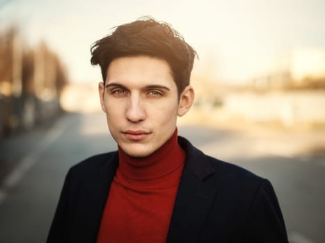 Handsome young man in city street, looking at camera with serious expression, wearing suit jacket and turtleneck