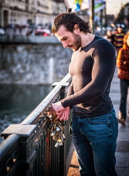 Side view of bearded man in casual clothes standing on footbridge and attaching love lock to metal railing