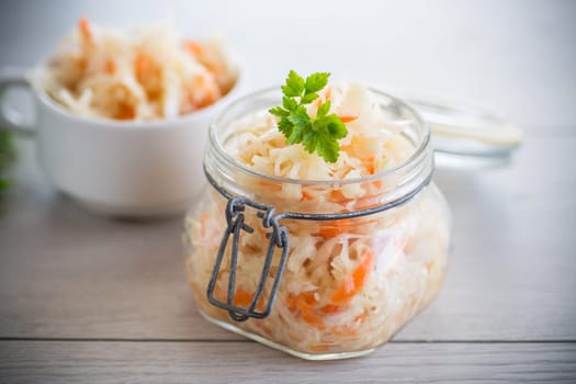 Sauerkraut with carrots and spices in a glass jar on a wooden table.