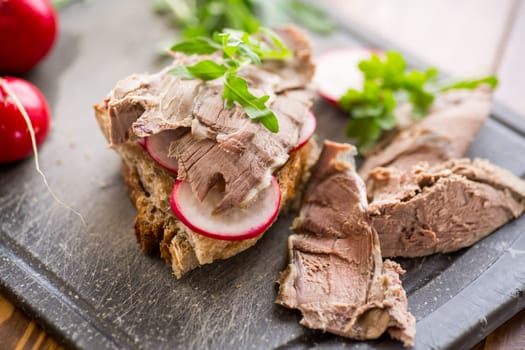 sandwich with baked meat, radish and herbs on a wooden table.