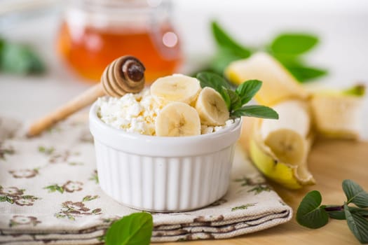 crumbly organic cottage cheese with honey and bananas in a ceramic bowl on the table