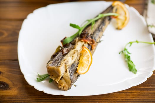 Baked fish with seasonings and spices in a plate on a wooden table