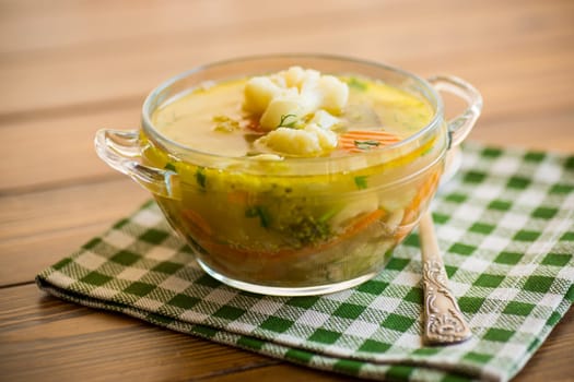 cooked chicken soup with cauliflower and vegetables in a bowl on a wooden table