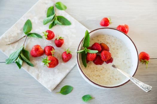 cooked diet oatmeal in a bowl with fresh ripe strawberries, on a wooden table.