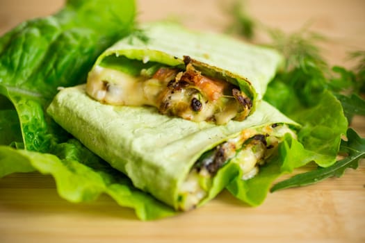 green hot vegetarian pita bread with mushrooms and different vegetables, with lettuce leaves on a wooden table.