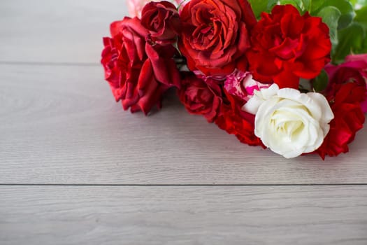Floral background of pink, red and other roses on a light wooden table
