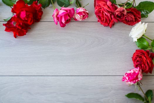 Floral background of pink, red and other roses on a light wooden table