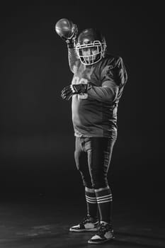 Portrait of a man in uniform for american football throws the ball on a black background. Monochrome