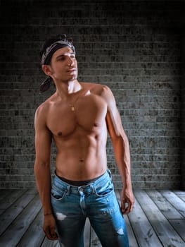 Sexy handsome young man standing shirtless in his empty room, looking up off-camera