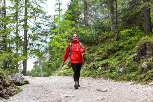 Free and happy alone. Cheerful woman hiking in the woods in red raincoat.