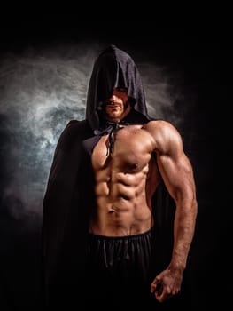 Scary muscular young man with pointed hood and cape on naked body